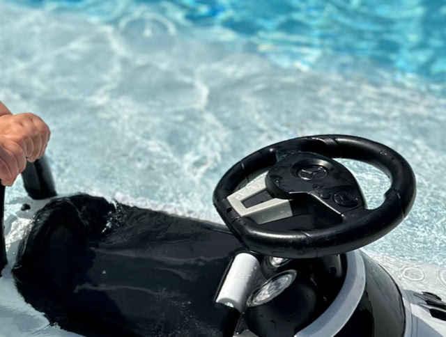 Ein Kind hält ein Lenkradspielzeug im Wasser eines Pools.